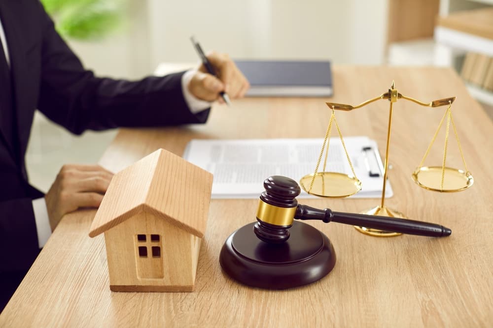 Lawyer at desk with scales of justice, gavel, and toy house, reviewing documents and signing contracts. Representing real estate law and legal services.
