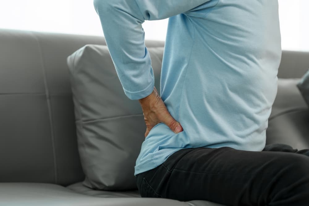 Man on couch, experiencing spinal discomfort, seeks relief from osteoporosis-related pain at home.