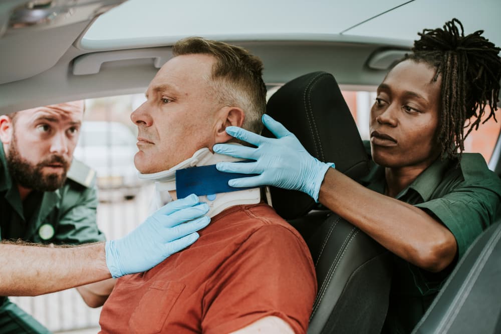 Paramedic providing medical care to an injured man involved in a car accident, securing a cervical collar.