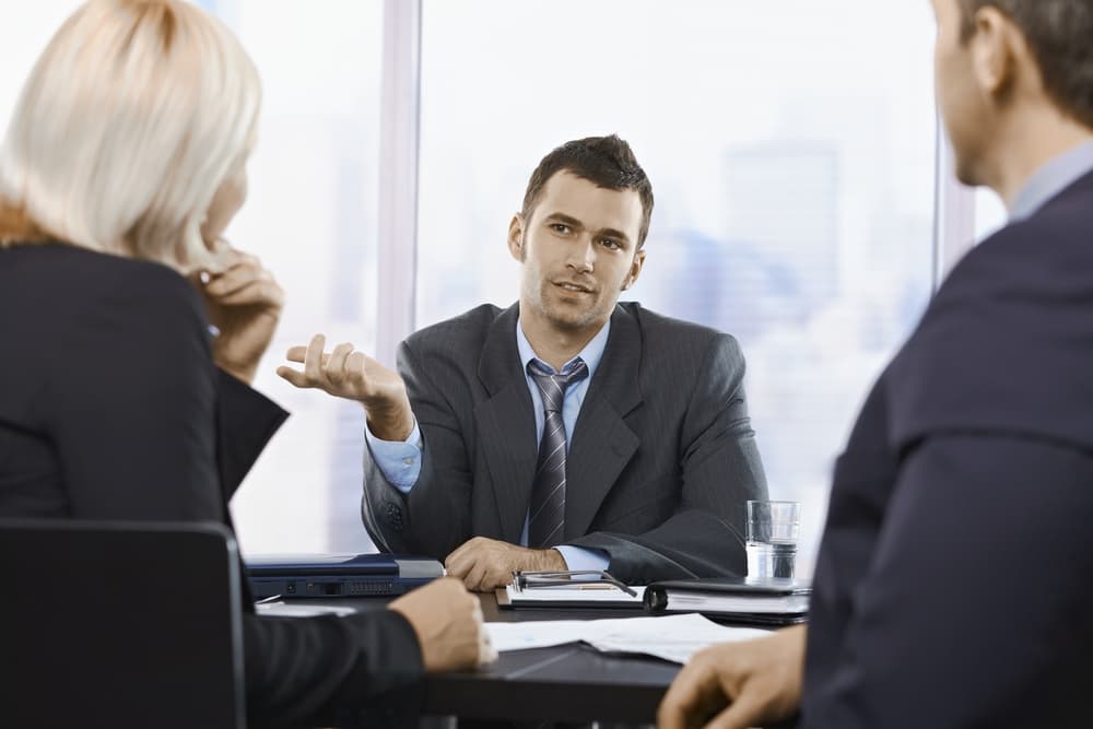 Colleagues engaged in a discussion about work in a busy office environment.