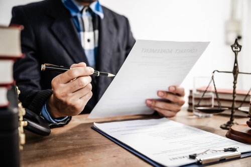Lawyer reviewing and explaining a legal contract at a wooden desk with scales of justice and legal books in the background.