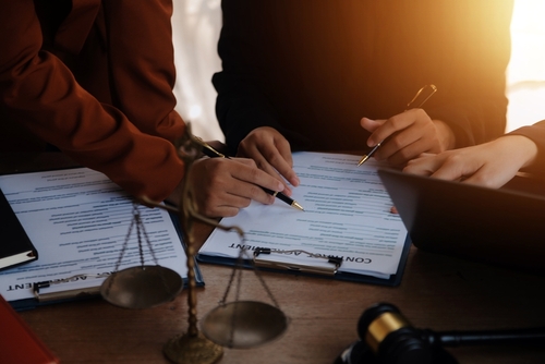 Two people reviewing and signing estate planning documents at a desk with a gavel and scales of justice in the foreground.