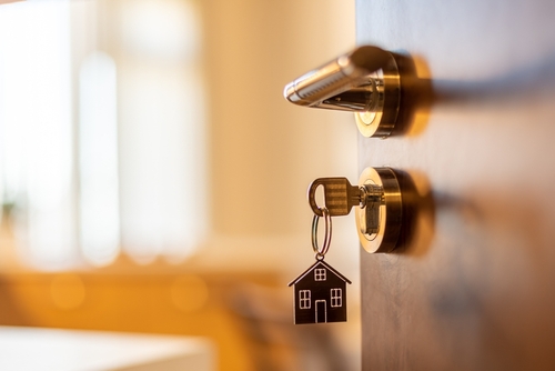 Close-up of a house-shaped keychain hanging from a key inserted in a modern wooden door.