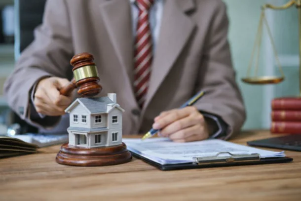 A lawyer sits at a desk with a model home, gavel, and contract documents.