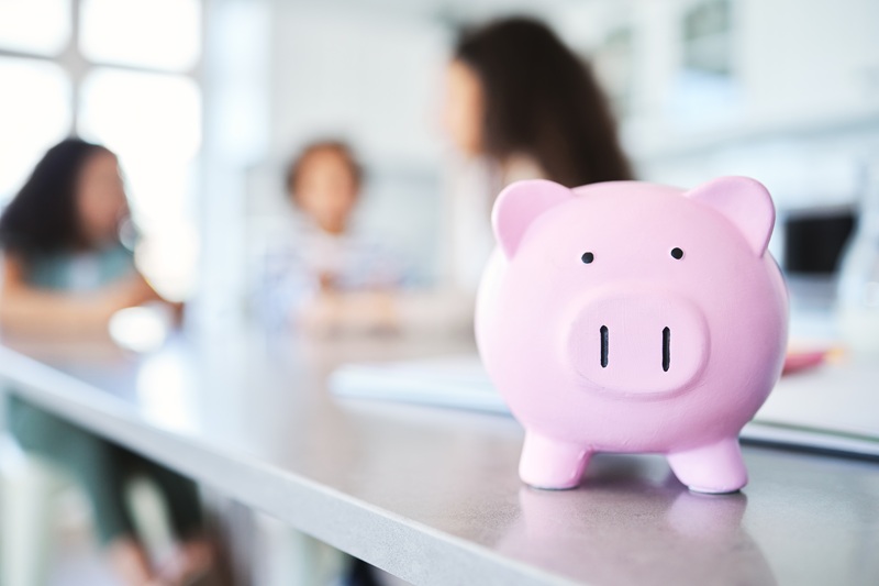 A piggy bank sits on a table with a family in the background discussing financial issues.