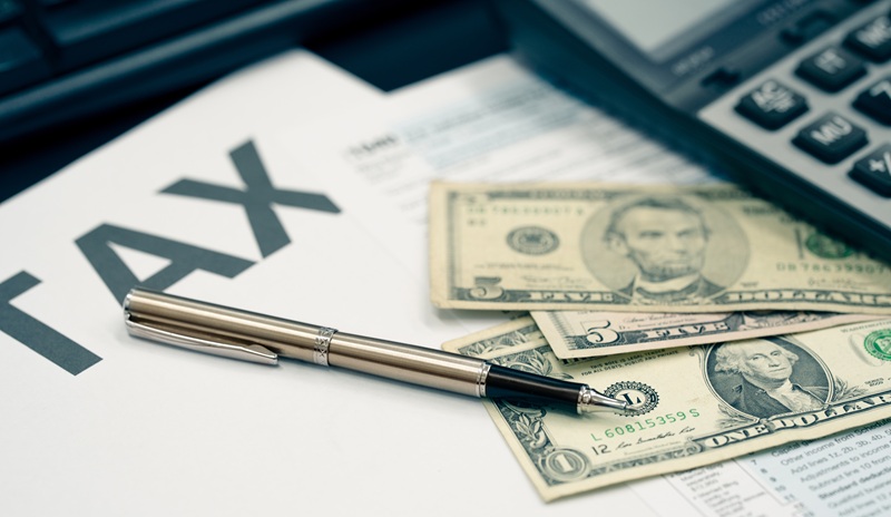 Tax documents, money, and a calculator on a desk. Businesses should ensure their employees are properly classified before tax season.